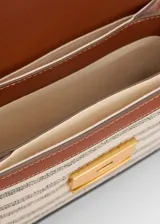 Bandolera rectangular de tela rayada en tonos beige y gris, con detalles en cuero marrón. Tiene correa larga ajustable, cierre con solapa y botón imantado, y herrajes dorados.