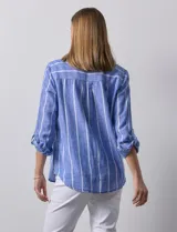 Camisa color beige con rayas verticales blancas, de lino, con cuello con solapa y abertura central con botones. Tiene un bolsillo aplicado en el pecho y mangas largas regulables con presilla y botón.