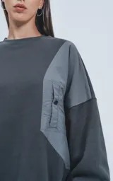 Buzo gris oscuro de cuello redondo, corte oversize y largo crop. Presenta un bolsillo grande de microfibra gris claro en el frente.