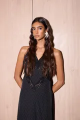 Vestido largo de seda color negro con estampado de lunares blancos. Presenta una silueta fluida, escote en V profundo con detalles de encaje y espalda descubierta con tiras cruzadas.