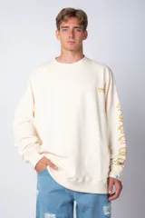 Buzo color crema de corte oversize con cuello redondo y puños y cintura acanalados. Presenta un pequeño logo bordado en el pecho y un estampado vertical con nombres de empanadas en la manga derecha.