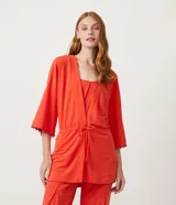 Kimono color naranja de tejido orly con mangas 3/4 con detalle de pompones en el dobladillo, lazo en la cintura y cierre frontal.