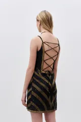 Vestido corto negro con lentejuelas doradas formando un patrón geométrico. Tiene breteles finos y escote recto.