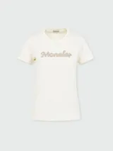 Camiseta blanca de algodón con cuello redondo y mangas cortas. Presenta el logo de la marca Moncler bordado con perlas en el centro del pecho.