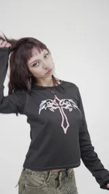 Remera corta negra de poliéster y elastano, con estampado de cruz rosa y alas blancas.