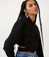 Camisa cropped negra de viscosa con cuello camisero, manga larga con puños abotonados, bolsillos de parche en el pecho, cierre frontal con botones ocultos, recortes laterales y elástico en la espalda.