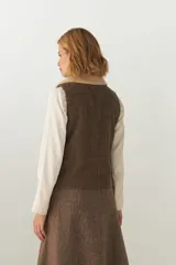 Chaleco corto color beige, de corte recto y abierto, con cuello de piel sintética blanca y apliques de cuero marrón en los bolsillos.