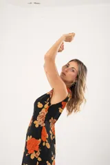 Vestido midi negro con estampado de flores naranjas y beige, espalda descubierta con tres botones en forma de flor, tajo lateral y flecos en el ruedo.