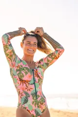Enterito de surf de lycra Ecocean reciclada con protección SPF 50, estampado con motivos de hojas y cactus en tonos rosa, verde y marrón. Tiene mangas largas con estampado geométrico en los antebrazos, escote en V y cierre frontal con cremallera.