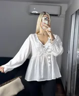 Blusa color crema con escote en V, mangas largas abullonadas con puños elásticos y detalles de encaje y bordado en el frente.