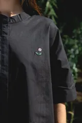 Camisa negra de algodón con cuello mao y mangas cortas. Presenta un pequeño bordado de una flor blanca en el pecho.