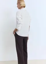 Camisa blanca de lino con cierre de botones, bolsillo de parche en el pecho, manga larga con puños abotonados, diseño recto y cuello camisero.
