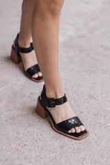 Sandalias negras de cuero con textura tipo cocodrilo, taco de madera y hebilla en la tira del tobillo.