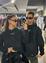 Hoodie negro de corte holgado con capucha y cordón ajustable. Estampado frontal con la leyenda "BE TRENDY EST. 2022" en color rosa.