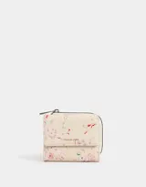 Billetera pequeña de cuerina color crema con estampado floral en tonos rosa y rojo. Tiene cierre de cremallera en la parte superior y solapa con broche a presión en la parte inferior.