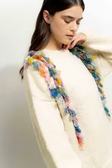 Sweater color crema de tejido de punto con cuello redondo y mangas largas. Presenta flecos de colores en los hombros.
