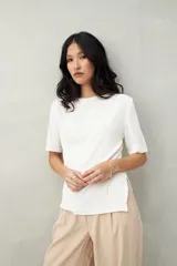 Remera blanca de tejido texturizado, con cuello redondo, mangas cortas y aberturas laterales.