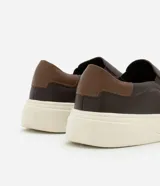 Championes slip on de cuero color marrón oscuro con detalle de cuero marrón claro en el talón y suela de goma color crema.