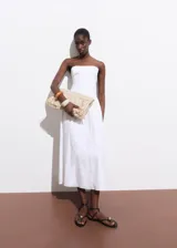 Vestido midi blanco sin mangas, con escote recto, detalle fruncido en los laterales y cierre de cremallera en la parte posterior.