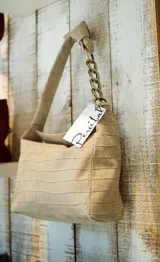 Cartera tipo bolso de mano color beige con textura símil piel de cocodrilo. Tiene correa corta de hombro con eslabones dorados.