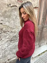 Sweater de punto grueso color borgoña con cuello alto y diseño de trenzas en el frente.