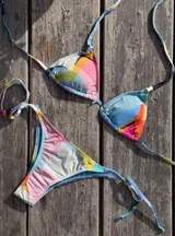 Conjunto de bikini con corpiño de triángulos movibles con almohadillas desmontables, que se ata al cuello y a la espalda. La bombacha es vedetina con tiritas a los costados para atar a medida de la cadera. Presenta un estampado abstracto con colores celeste, rosa, amarillo, naranja y blanco.