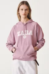 Sudadera color borgoña con capucha ajustable con cordones, manga larga y estampado dorado en el frente con el texto "A Coruña" y un escudo.