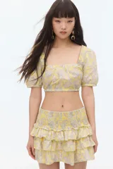 Blusa cropped de algodón color amarillo con estampado paisley en tonos grises. Tiene escote cuadrado elástico, mangas cortas con puños ajustados, espalda descubierta y tiras para atar.