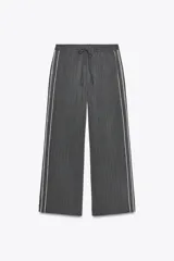 Pantalón de tiro alto negro a rayas verticales blancas, con cintura elástica ajustable con cordones, bolsillos delanteros y banda lateral blanca.