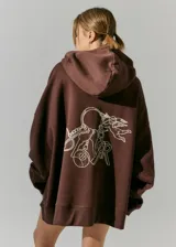 Buzo marrón de frisa con capucha y bolsillos delanteros. Corte oversize, recortes laterales y doble cordón con puntera de goma. Estampa en frente y espalda realizada en serigrafía con diseño de llavero con dijes.