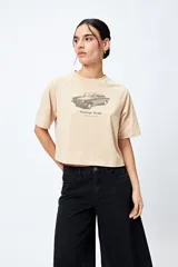 Remera cropped blanca de mangas ranglan con estampa frontal de un auto antiguo y texto "Vintage Gems / retro car club".