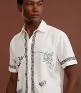 Camisa de manga corta confeccionada en algodón y lino, color blanco con bordado floral en negro.