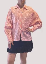 Camisa oversize de lino color rosa pálido con finas rayas verticales blancas. Presenta cuello camisero, cartera con botones de nácar y puños con tablitas.