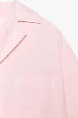 Camisa corta color rosa claro, confeccionada en algodón. Tiene cuello solapa de muescas, manga corta, bolsillo de plastrón en el pecho, bajo recto y cierre frontal con botones.