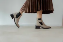 Botines Chelsea color beige con elásticos laterales negros, punta cuadrada, detalle de hebilla lateral y tacón bloque bajo.