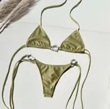 Conjunto de bikini color verde oliva (pistacho) compuesto por un corpiño triangular con argolla central y una bombacha colaless con tiras laterales ajustables y argollas laterales. Las argollas son de zamak.