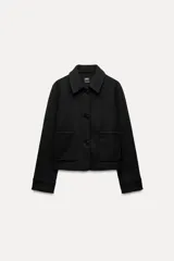 Chaqueta corta negra de cuello solapa y manga larga con puños. Tiene bolsillos de parche en el frente y cierre frontal con botones.