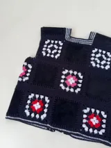 Chaleco sin mangas, confeccionado con cuadrados de cuero negro perforado combinados con cuadrados de crochet en hilo de algodón negro y blanco, con detalles centrales en rojo.