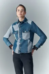 Campera de denim rígido con recortes en diferentes tonos de azul, corte recto, cuello camisero, cierre frontal con botones metálicos, bolsillos con solapa y botones en el pecho, y mangas largas con puños abotonados.