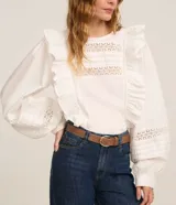 Blusa blanca de tricolina con volados en los laterales, cuello redondo, cierre por gota, mangas abullonadas largas y entremedios en el busto y en las mangas.