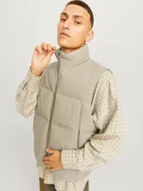 Chaleco acolchado sin mangas color gris topo, con cuello alto y cierre de cremallera. Tiene bolsillos frontales y relleno de fibra sintética.