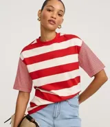 Remera de algodón con cuello redondo, cuerpo a rayas horizontales anchas rojas y blancas, y mangas cortas con rayas horizontales finas rojas y blancas. Presenta sisa desplazada y costuras aparentes.