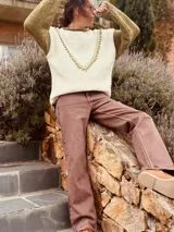 Sweater color crudo con mangas largas color verde oliva. Presenta cuello redondo y detalle de bordado con pompones en forma de V en el frente.