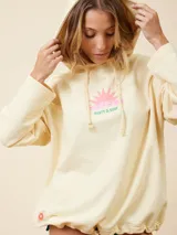 Canguro cropped color crema con capucha y cordón ajustable en la cintura. Estampado de un sol en el pecho.