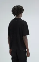 Remera negra de tejido de punto con moldería oversize, confeccionada en viscosa y poliéster. Presenta un diseño de malla con pequeños agujeros y un dobladillo acanalado.