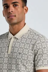 Polo de manga corta color beige claro con cuello y tapeta de botones en color crema liso. El cuerpo de la prenda presenta un estampado jacquard geométrico repetitivo de círculos interconectados en tono oscuro.