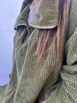 Buzo de pana fina color verde oliva, con diseño de corte holgado y mangas largas. Presenta una textura de cordón vertical característica de la pana y un pequeño parche decorativo en la parte superior de la espalda.