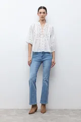 Blusa color verde oliva de manga 3/4 con volumen, cuello mao con abertura en V y botones. Presenta bordados y detalles de broderie calado en el canesú frontal y en las mangas. El cuerpo tiene un corte peplum con frunces.