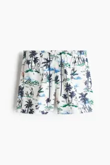 Short de baño blanco con estampado de palmeras, personas y paisajes en tonos azul, verde y rosa. Tiene cintura elástica con cordón ajustable, bolsillos laterales, bolsillo trasero con velcro y suspensor interior de malla.