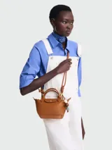 Bolso Longchamp modelo Le Pliage Ceramique XS, de cuero color caramelo, con doble asa corta y correa larga ajustable. Incluye charm colgante de cuentas de madera y cierre con broche a presión.